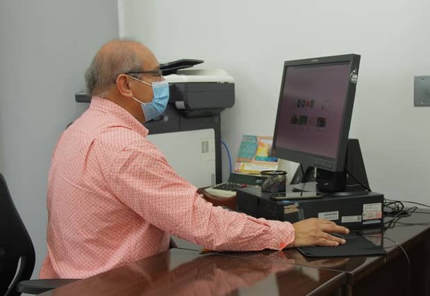 Hombre con tapabocas, sentado y trabajando frente a computador de escritorio