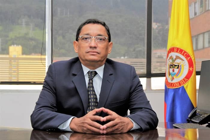 Fotografía del director de Función Pública, Nerio Alvis Barranco. Se ve sentado de frente, con sus manos sobre el escritorio y al fondo la bandera de Colombia
