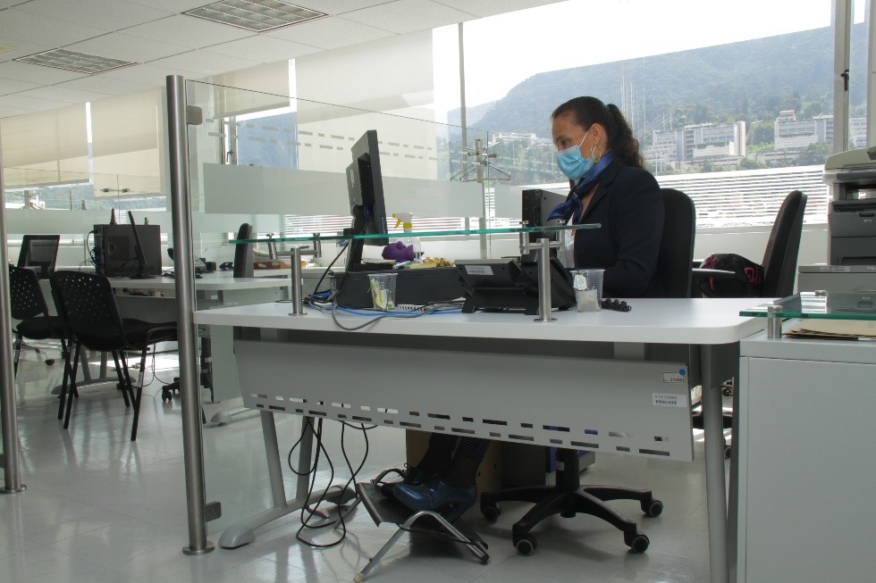 Mujer con tapabocas sentada en un puesto de trabajo frente a un computador