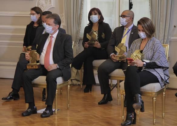 Se observa un grupo de seis personas sentadas, cada una sosteniendo sobre su regazo el trofeo de ganadores del Premio Nacional de Alta Gerencia
